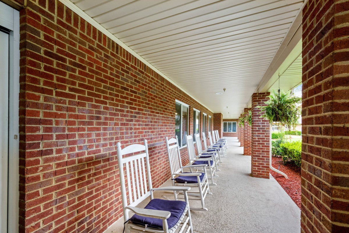 A row of rocking chairs on a covered porch with a brick exterior.