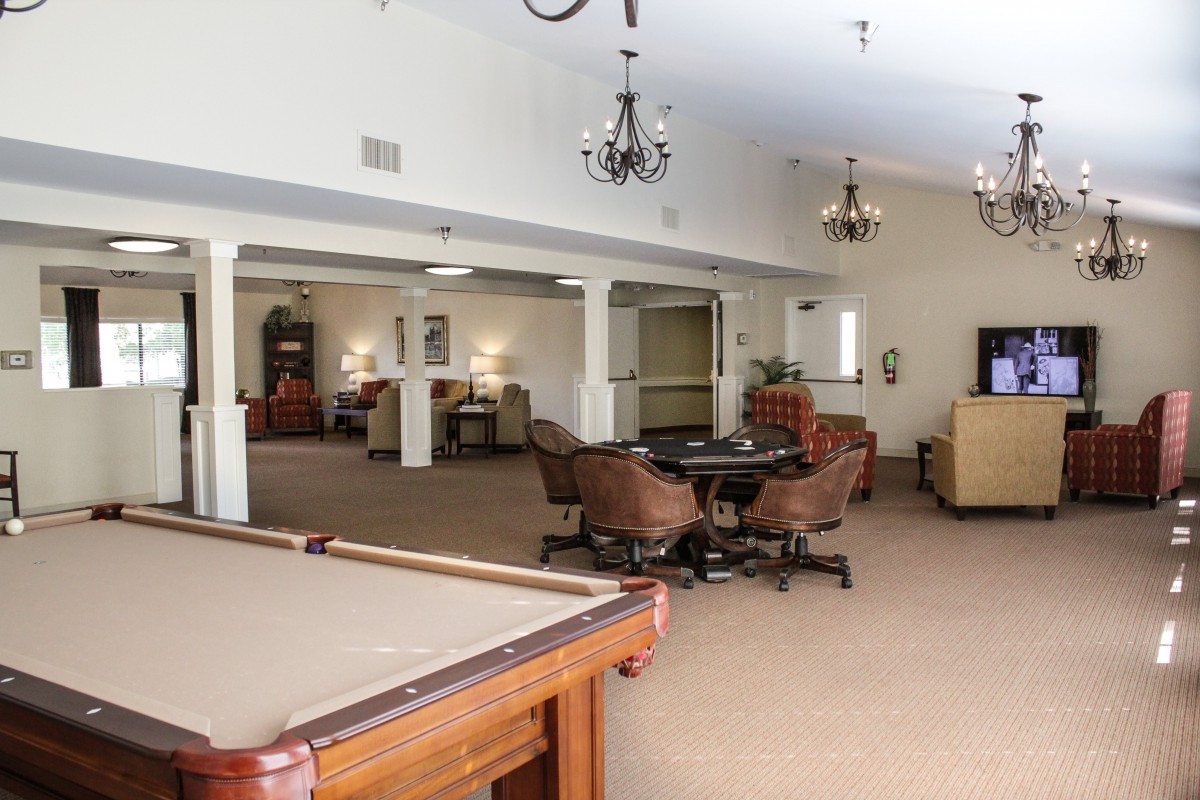 A spacious lounge area featuring comfortable seating, a billiards table, and decorative chandeliers.