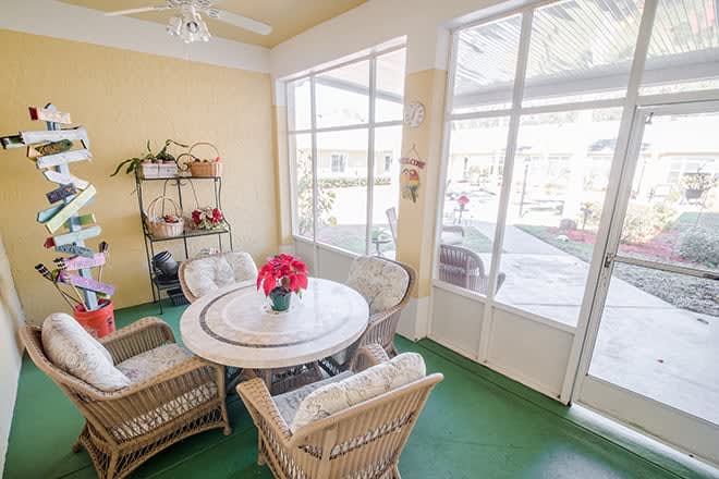 A bright sunroom featuring a round table with wicker chairs and large windows letting in natural light.
