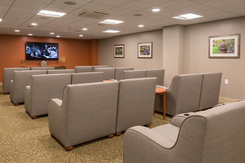 A waiting room with rows of gray chairs facing a television on the wall.