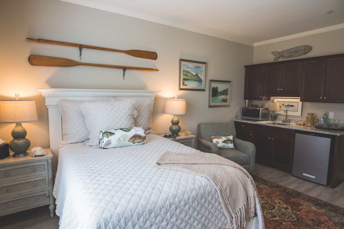 A cozy bedroom with rustic decor, featuring a neatly made bed, decorative oars on the wall, and a small kitchenette.
