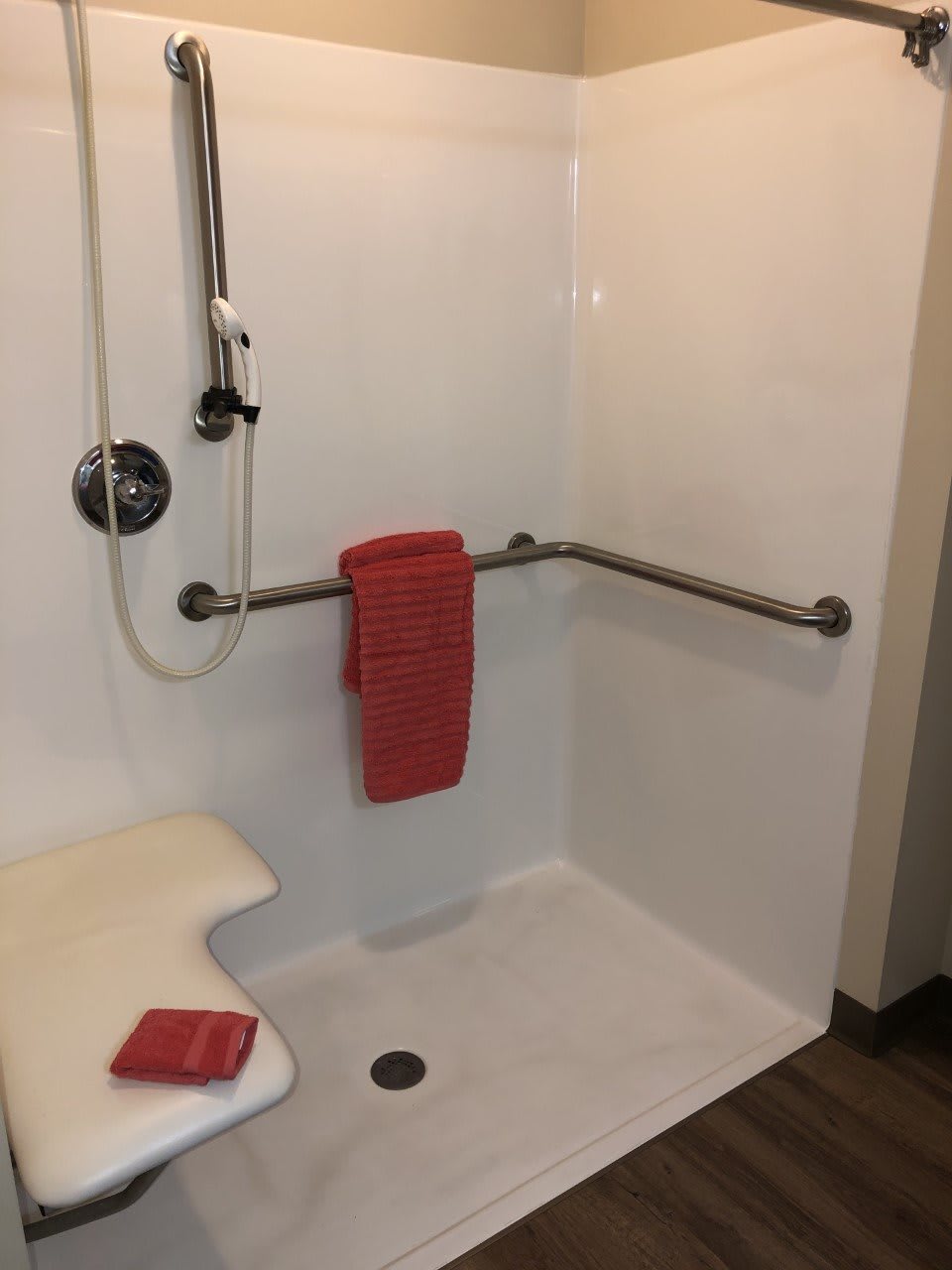 A bathroom with an accessible shower featuring a grab bar, showerhead, and red towels.