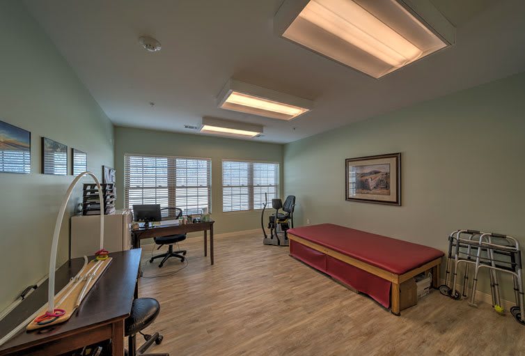 A well-lit office space with a desk, chairs, exercise equipment, and large windows.