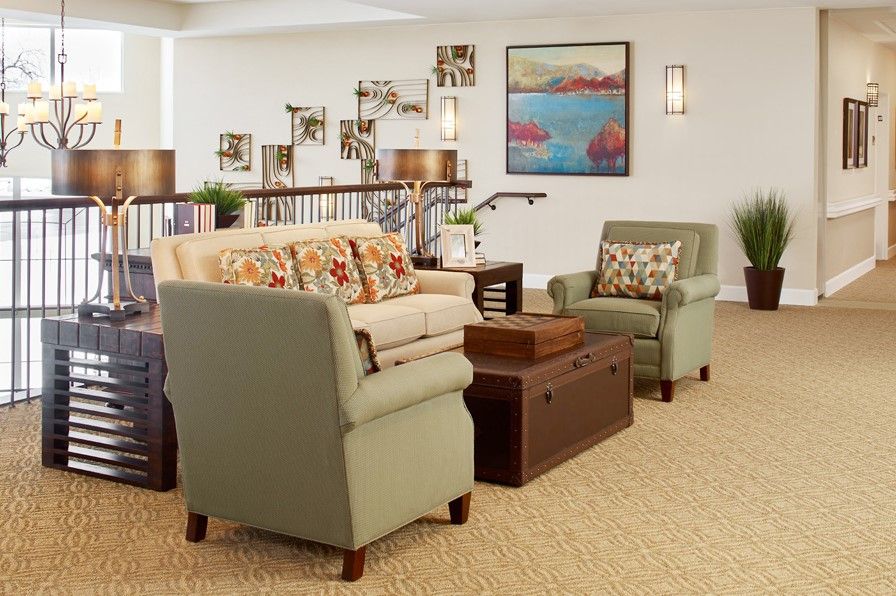 A cozy living room with a sofa, two armchairs, and a wooden coffee table. The walls are adorned with art and bookshelves filled with decor.