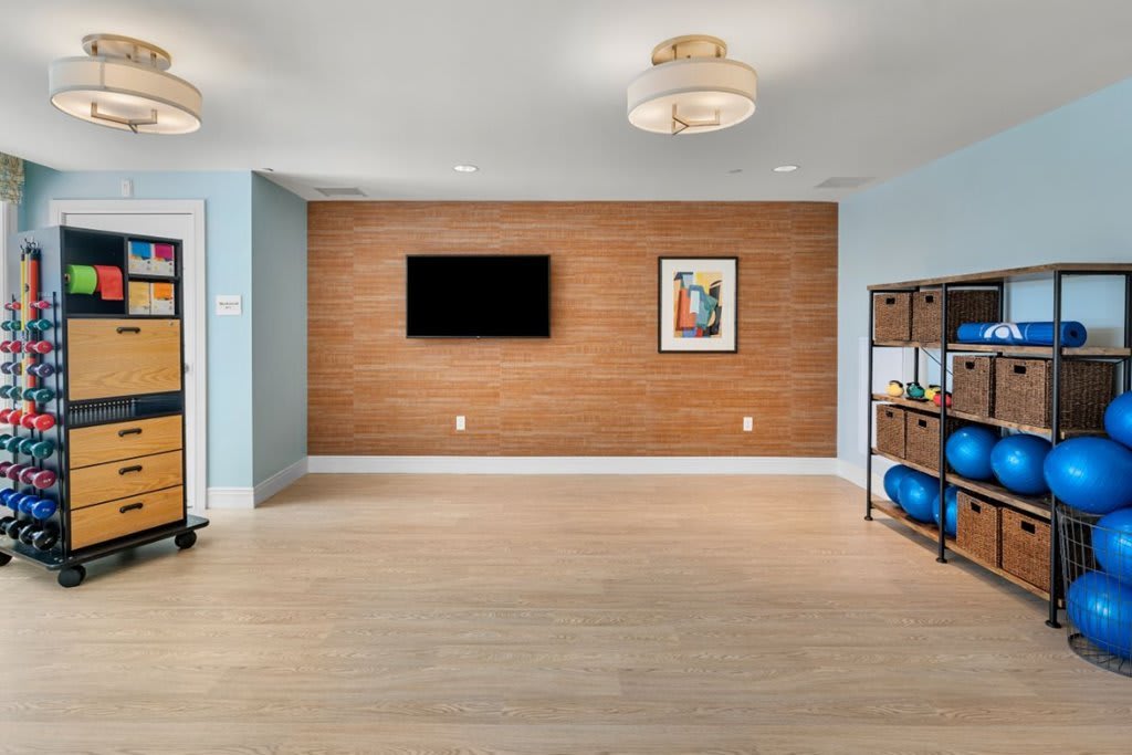 A modern living room with wood paneling, featuring a mounted TV and artwork on the wall, alongside a shelf with exercise equipment.
