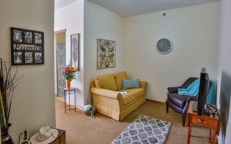 A cozy living room with a yellow sofa, an armchair, decorative artwork, and a colorful bouquet of flowers.
