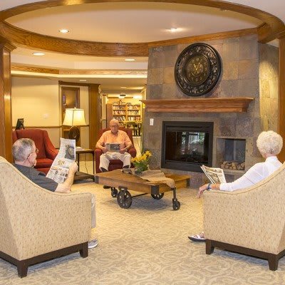 A cozy living room with a fireplace, where three people are relaxing in comfortable armchairs.