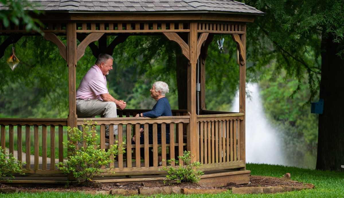 A man and woman talking in a gazebo by a fountain in a park.