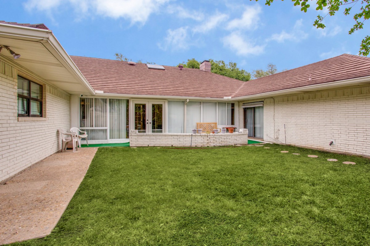 A view of a residential backyard featuring a well-maintained lawn and patio area.