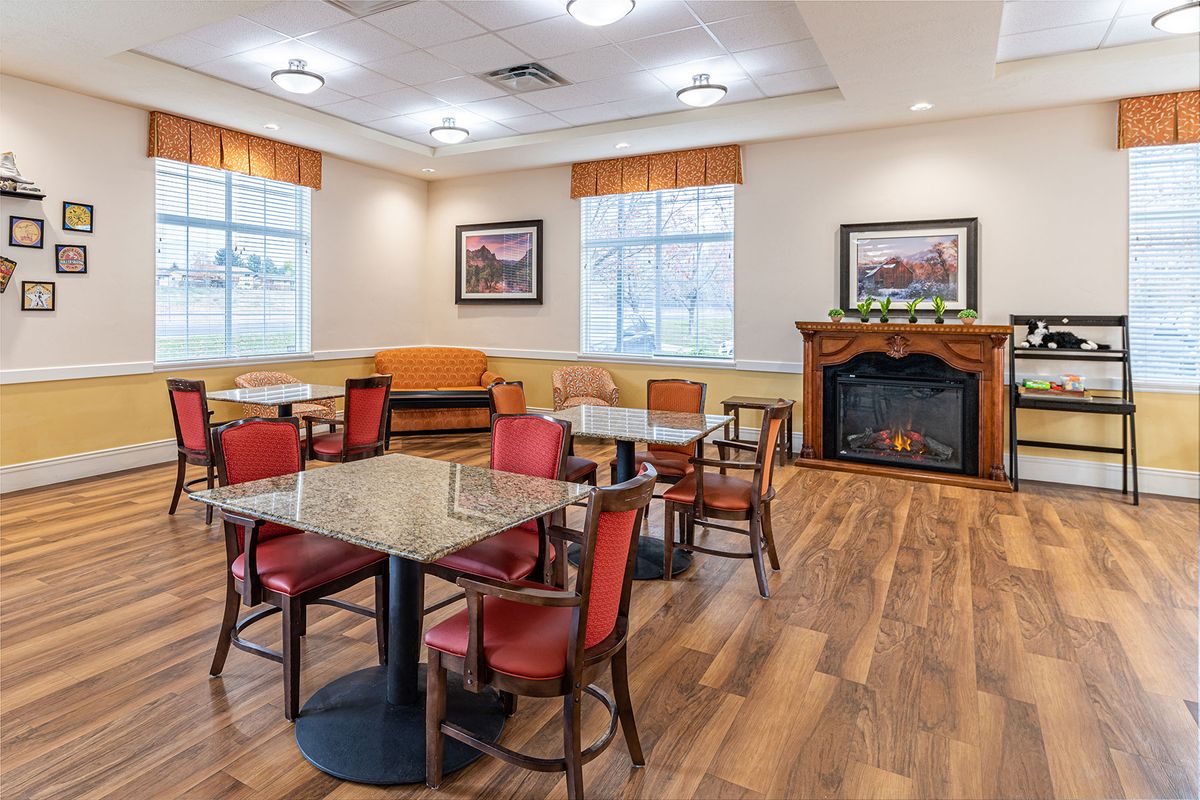 A cozy dining area with tables and chairs, featuring a fireplace and wood flooring.