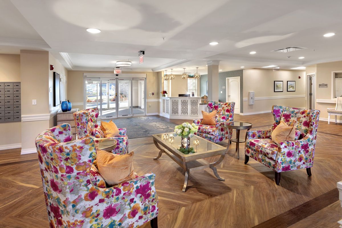 A bright and inviting living room with floral patterned chairs, a central coffee table, and a wooden floor.