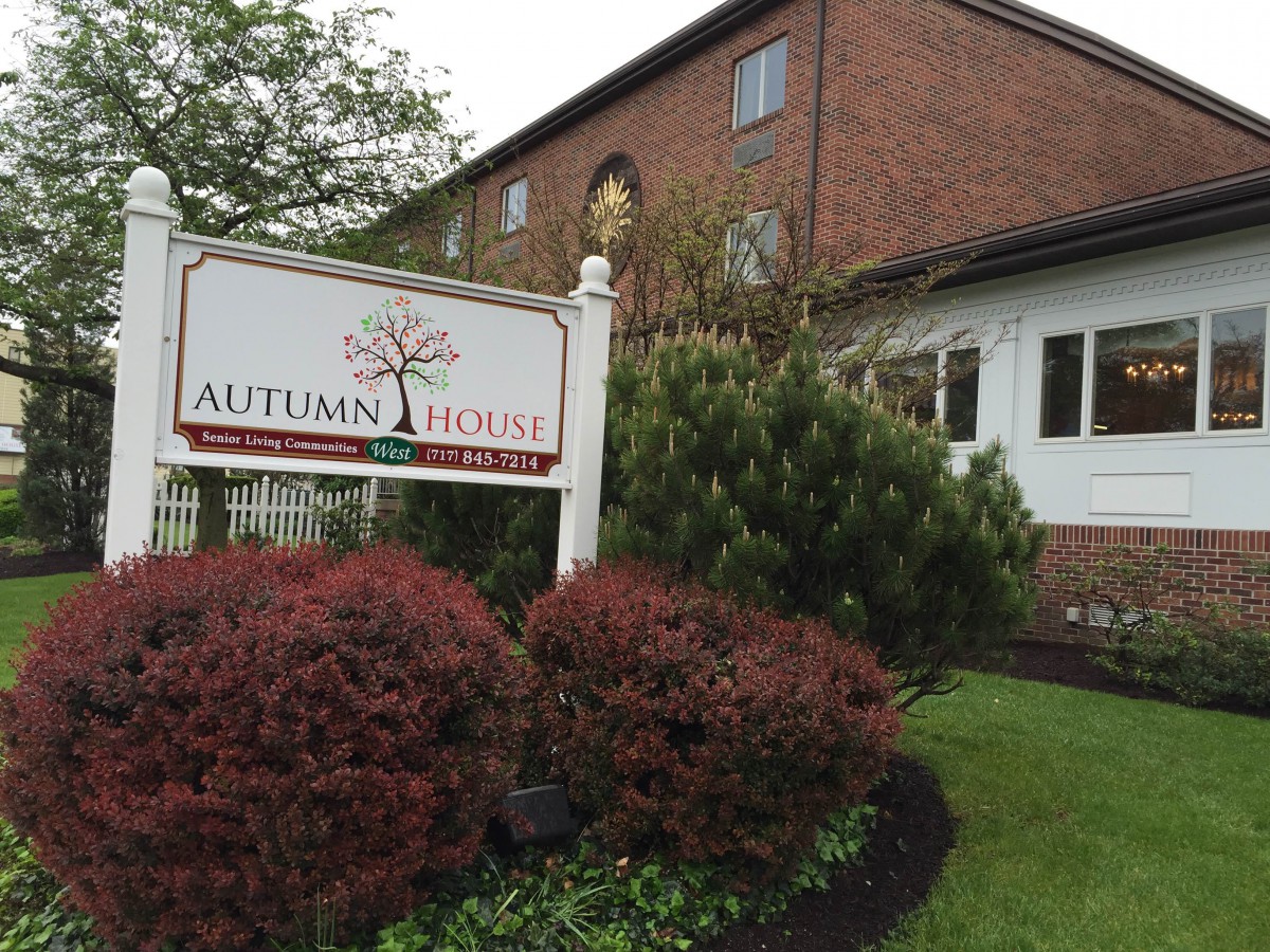 A brick building with a sign reading 'Autumn House' surrounded by well-maintained bushes and trees.
