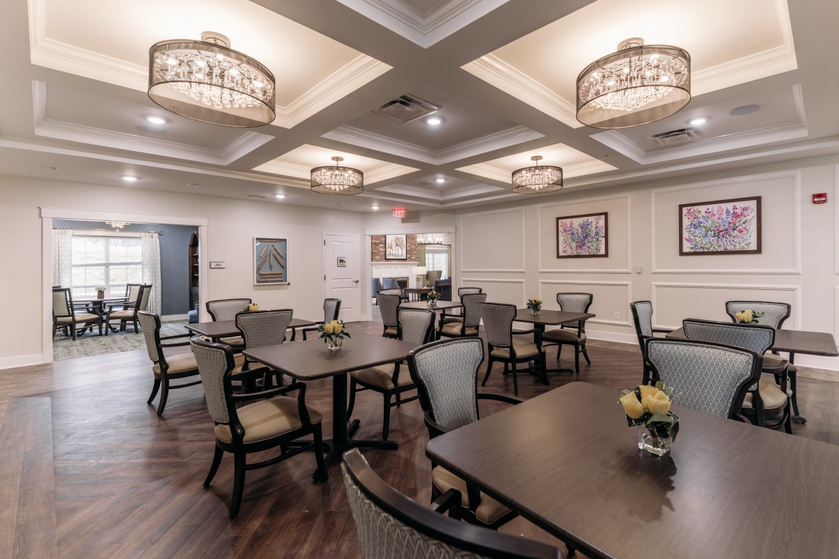 An elegant dining room with neatly arranged tables and chairs, featuring decorative lighting and a coffered ceiling.