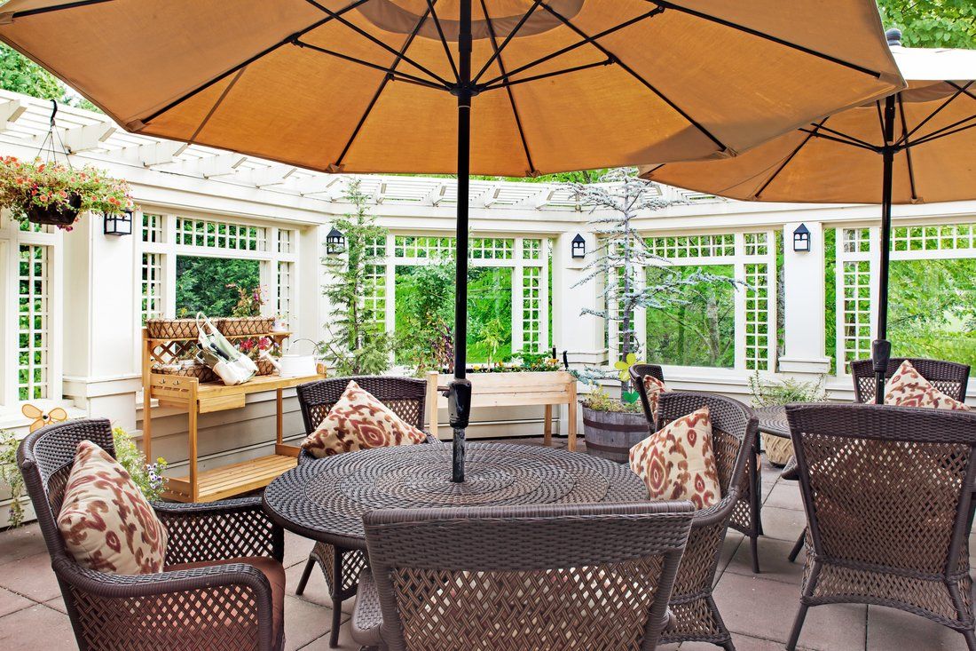 A cozy outdoor patio setting with a round table, cushioned chairs, and a large umbrella offering shade.