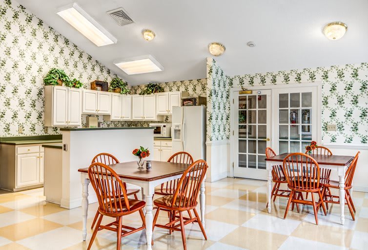 A spacious kitchen with a dining area featuring wooden chairs and tables, bright cabinets, and patterned wallpaper.