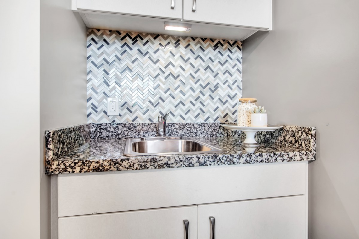 Modern kitchen sink with granite countertop and stylish chevron-patterned backsplash.