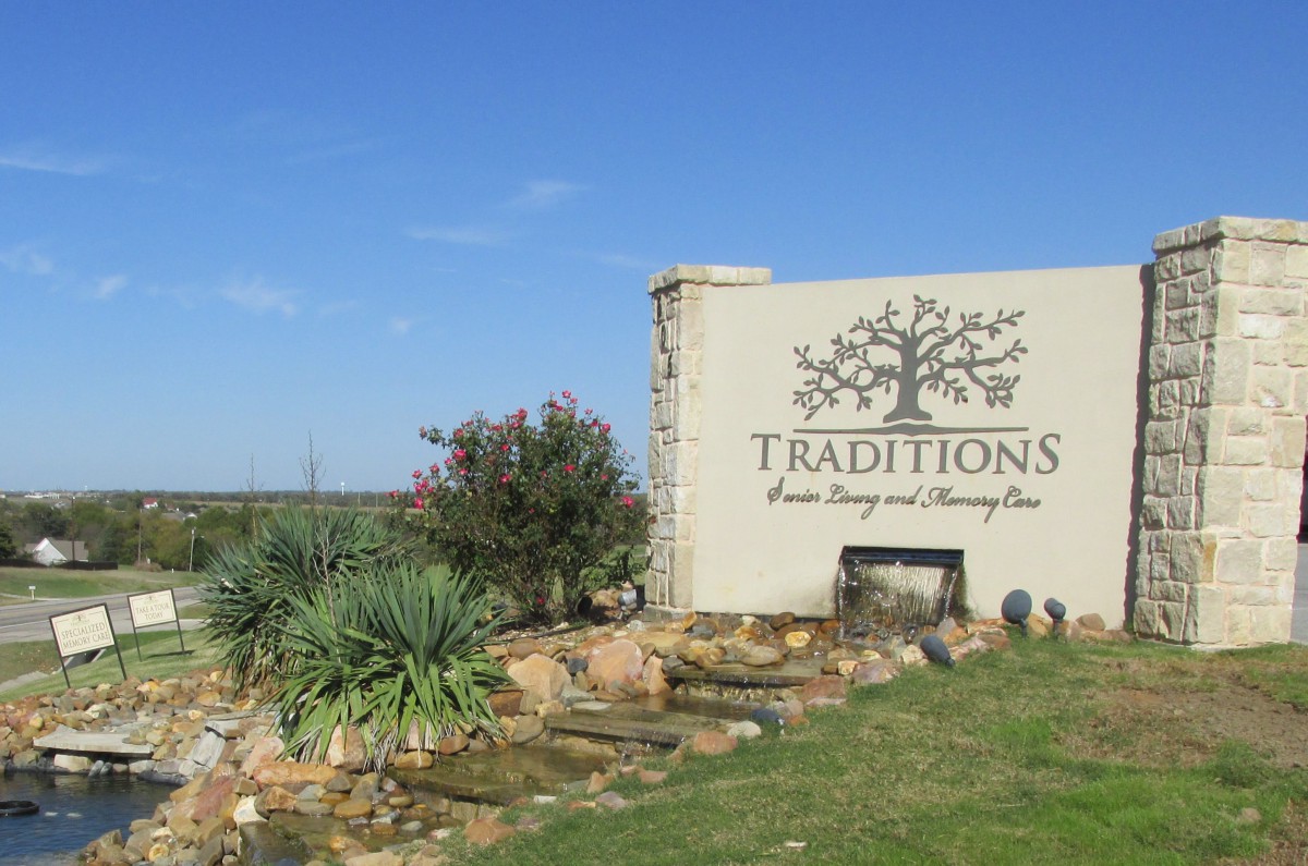 Entrance sign for 'Traditions' with natural landscaping and blue sky.