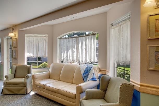 A cozy living room with comfortable seating, large windows, and sheer curtains allowing sunlight to stream in.
