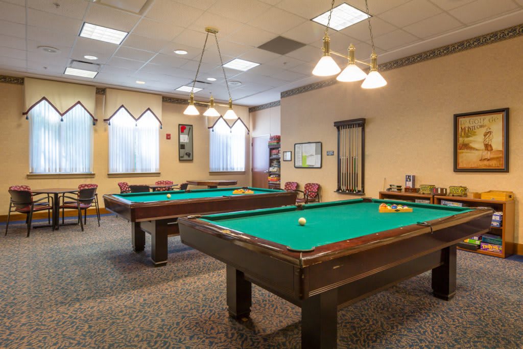 A well-lit recreation room with multiple pool tables and seating.