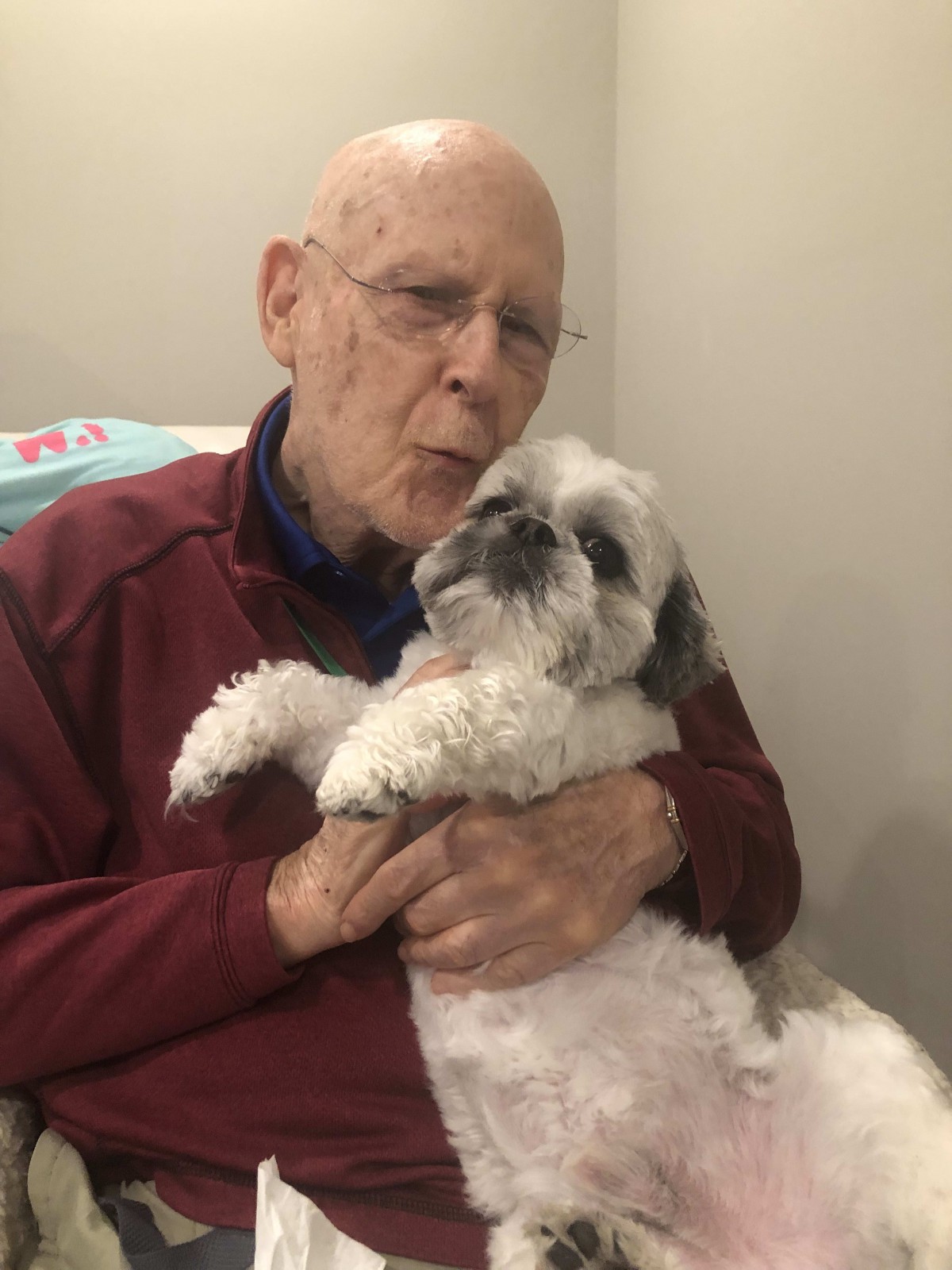 An elderly man holding a dog affectionately indoors.