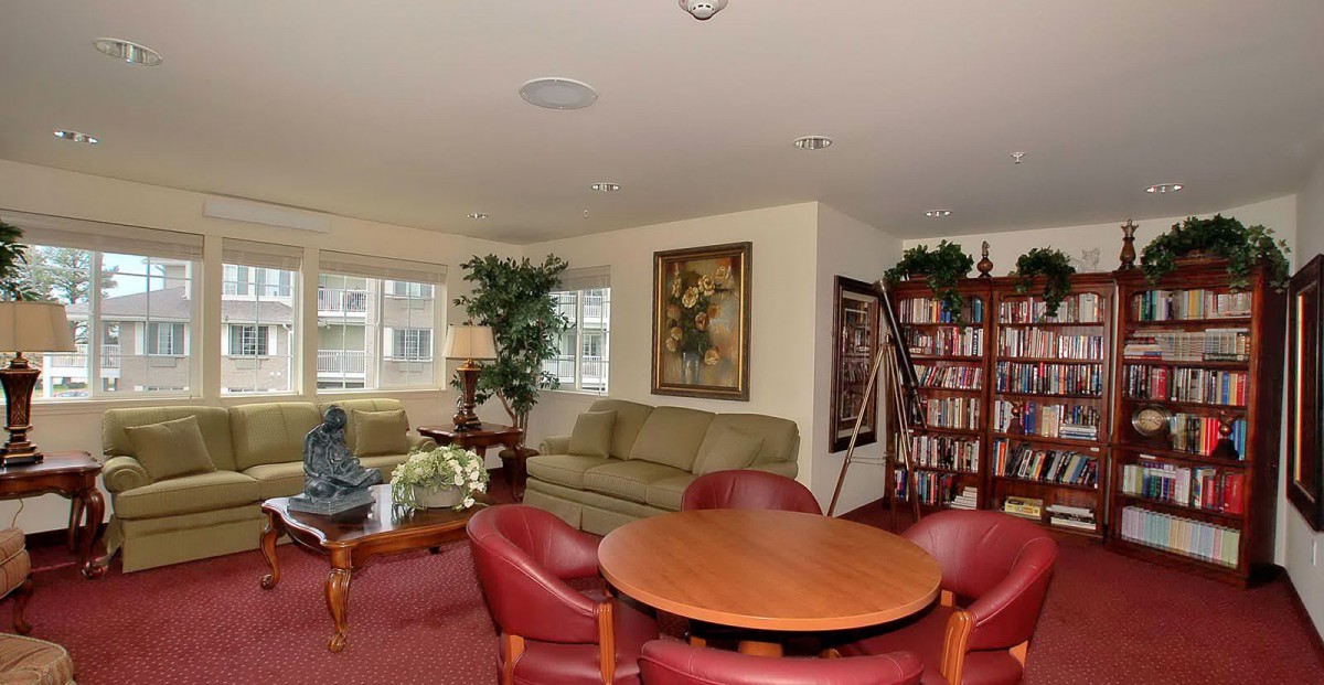 A cozy living room with a sofa, bookshelf, round table surrounded by chairs, and decorative plants.