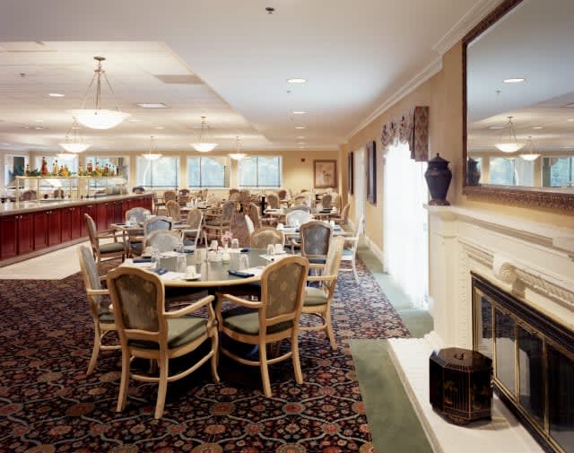 An elegant dining room interior with tables and chairs, featuring a fireplace and decorative carpeting.