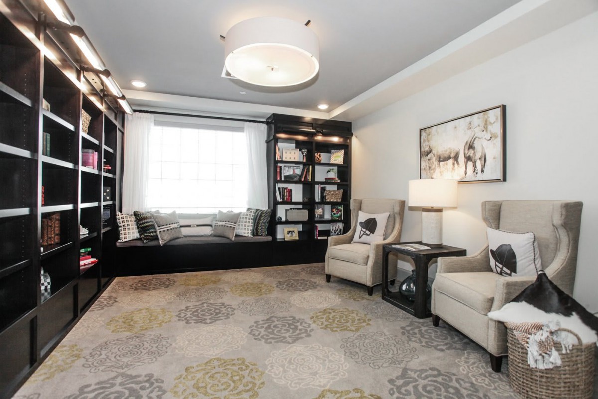 A cozy, modern living room with bookshelves, a window seat, and comfortable armchairs.