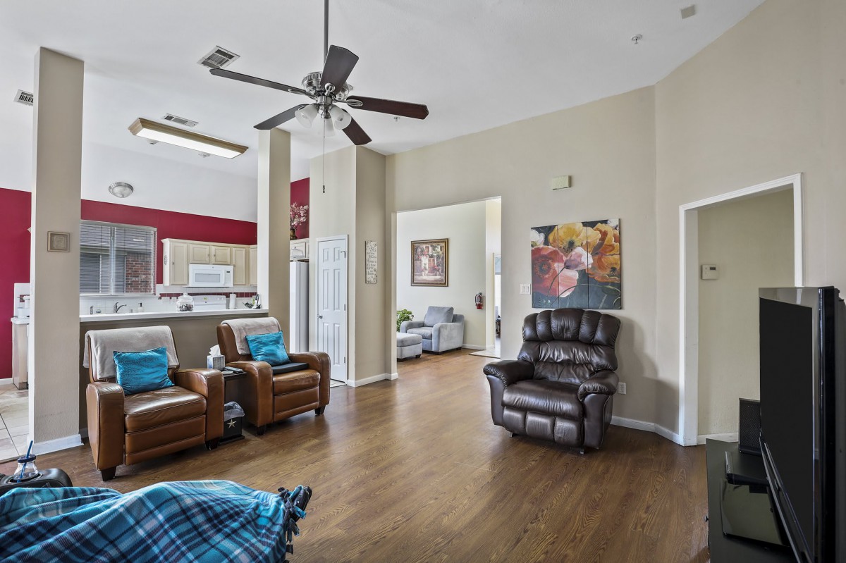 A cozy living room with comfortable seating and a ceiling fan, featuring wood flooring and colorful artwork.