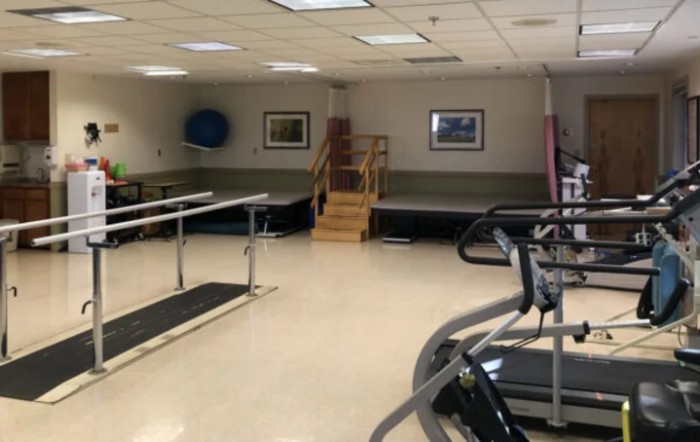 A physical therapy room equipped with parallel bars, exercise machines, and wooden stairs for rehabilitation exercises.