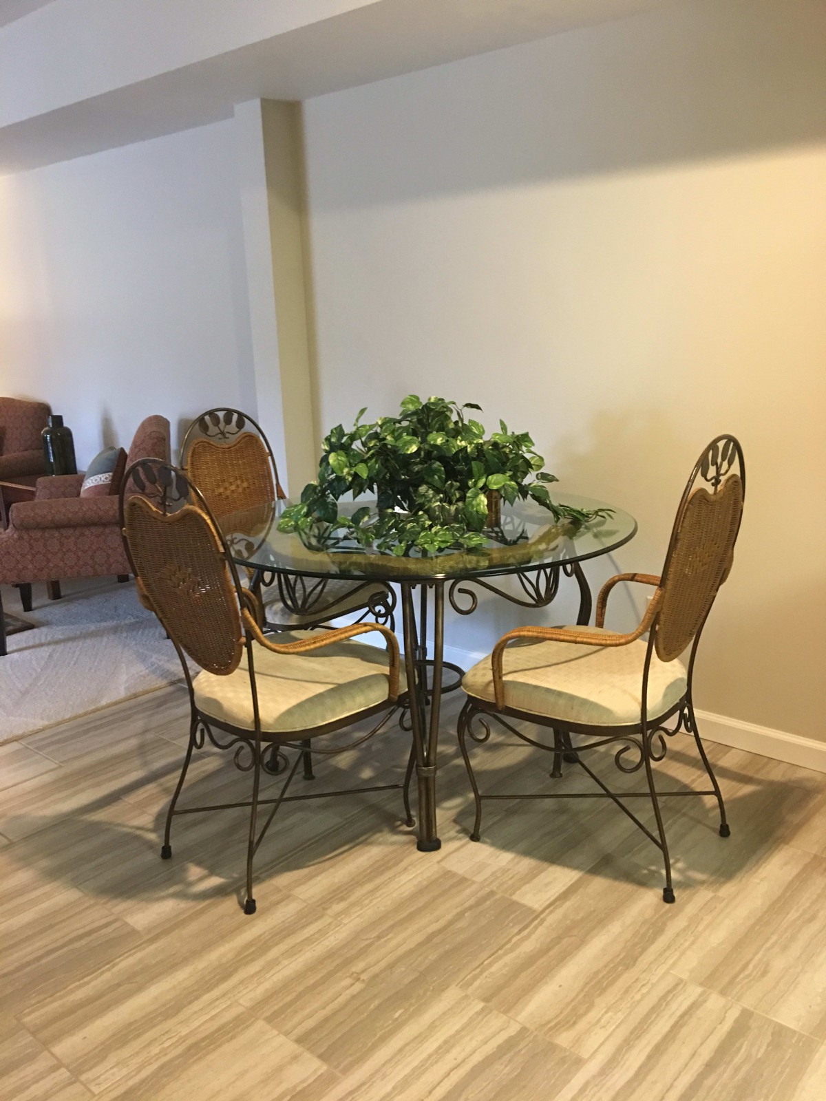 A cozy dining area featuring a glass table with decorative indoor plants and wicker chairs.