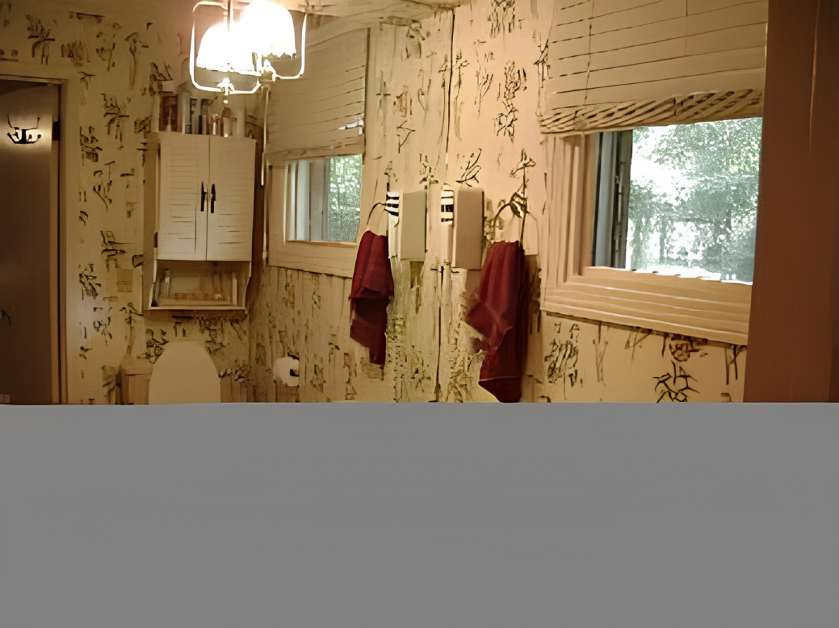 A vintage-style bathroom featuring floral wallpaper, a mirror, red towels, and a window with blinds.