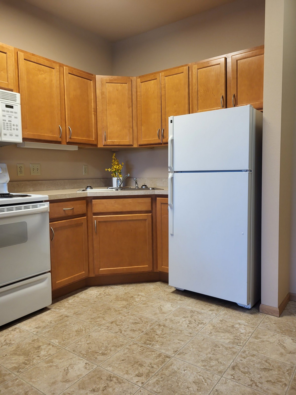 A modern kitchen with wooden cabinets, a refrigerator, oven, microwave, and sink.