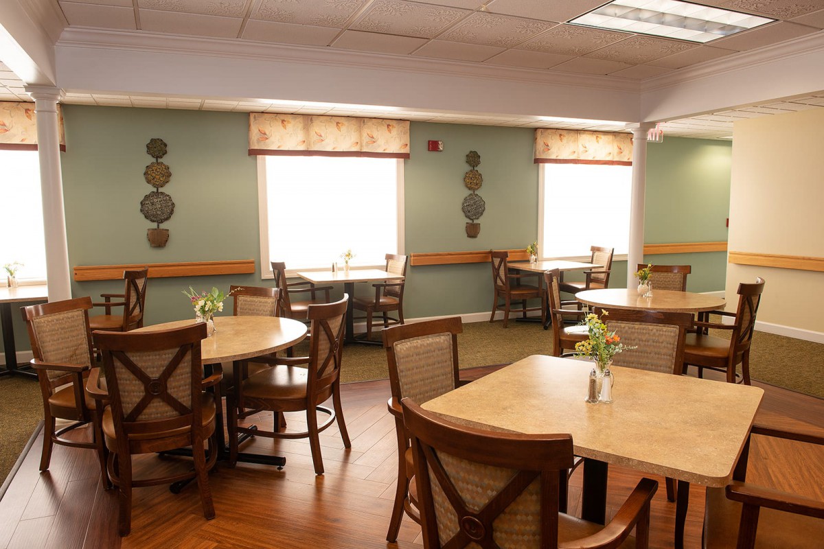 An empty dining room with wooden tables and chairs, decorated with wall ornaments and natural lighting from the windows.