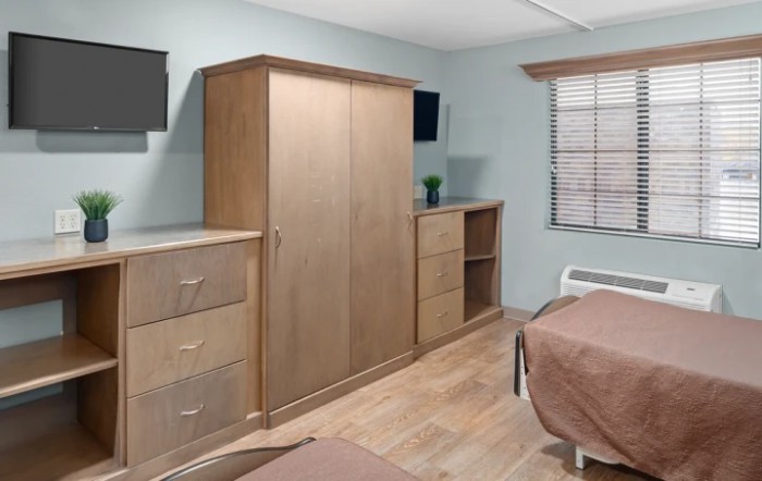 A minimalist bedroom featuring wooden furniture with a wardrobe, dresser, and bed.