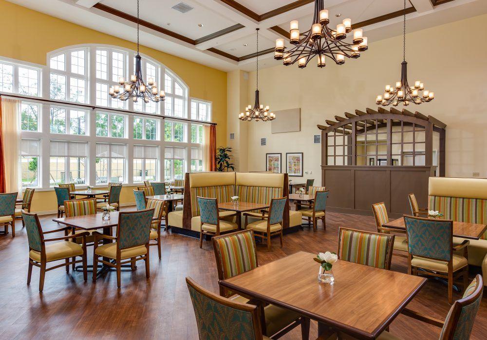 An elegant dining area with wooden tables, upholstered chairs, and large windows providing natural light.