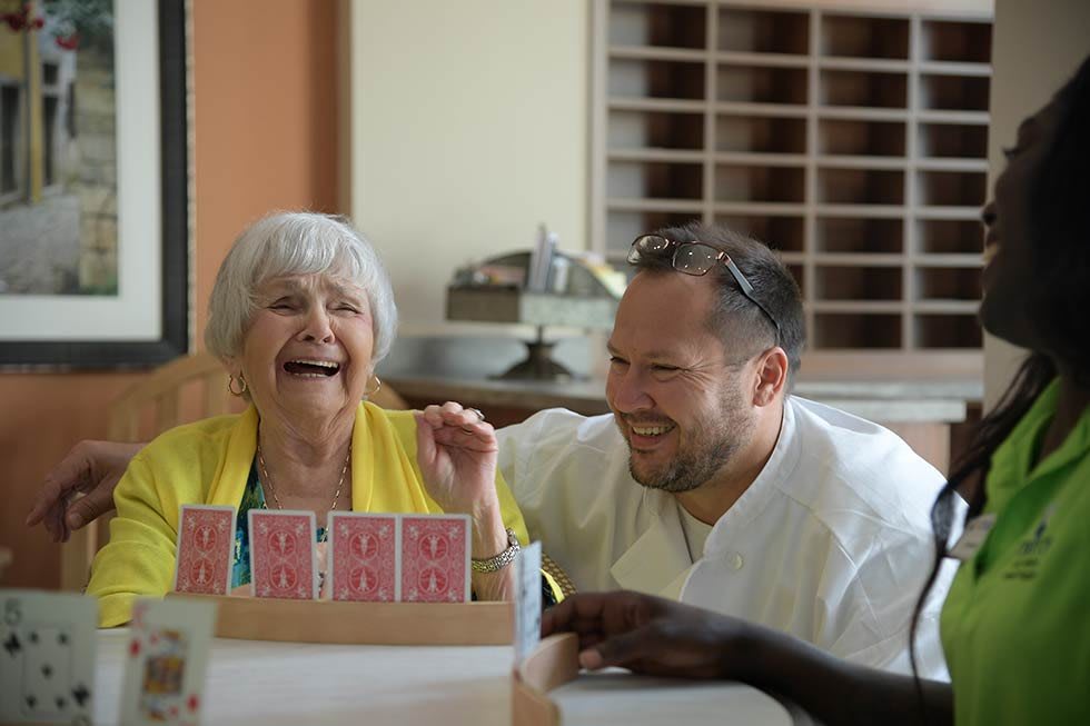 A joyful moment as an elderly woman and a man share a laugh while playing cards.
