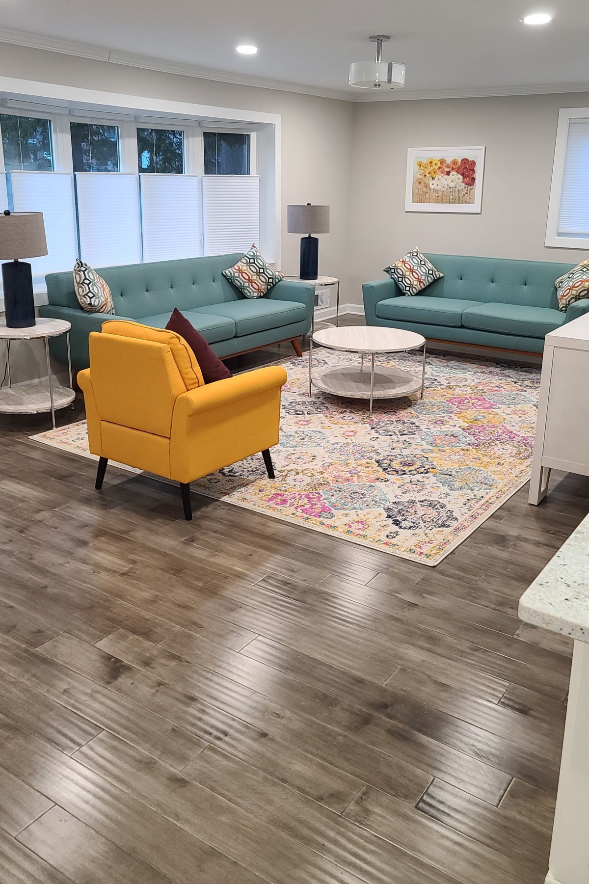 A modern living room with teal sofas, a yellow armchair, a colorful rug, and wood flooring.