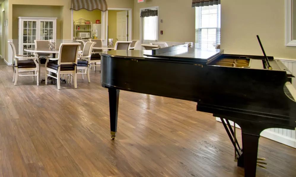 A spacious music room featuring a grand piano with wooden floors and seating area.