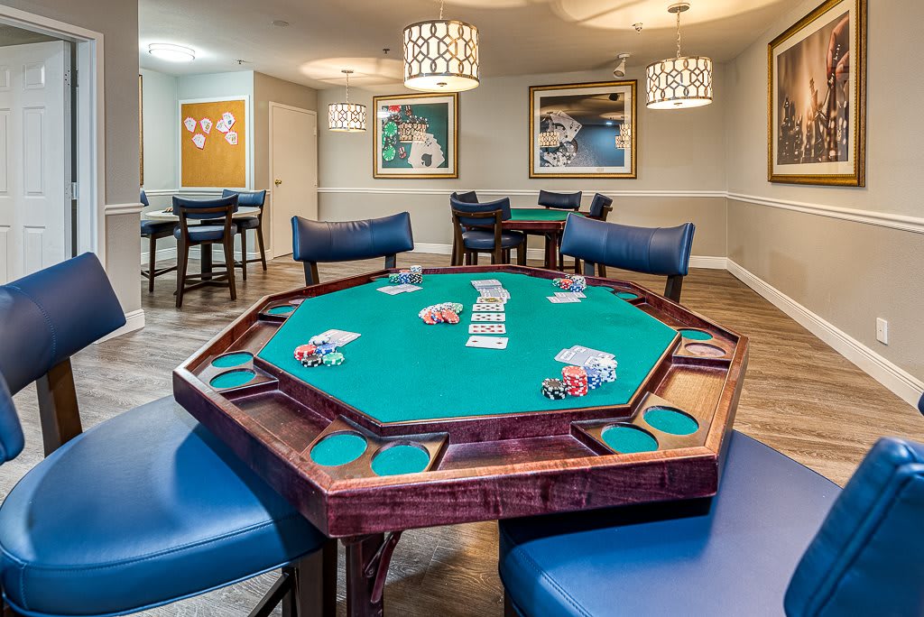 A game room featuring a poker table with cards and chips neatly arranged, surrounded by blue chairs.