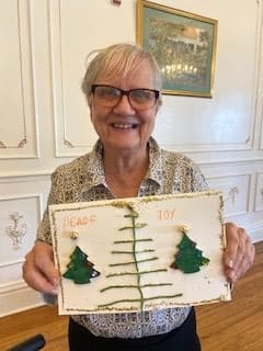 A person smiling and holding a crafted artwork featuring trees.