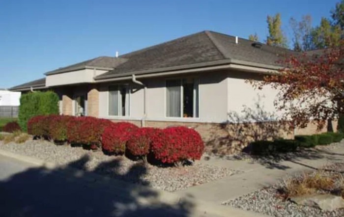 A suburban house with landscaping featuring red bushes on a sunny day.