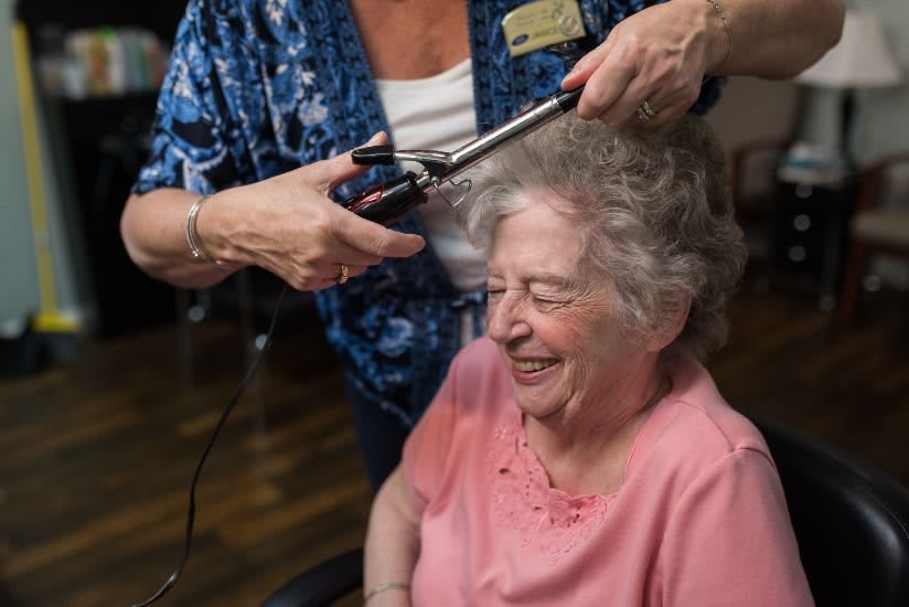 A senior woman smiling while having her hair styled with a curling iron.