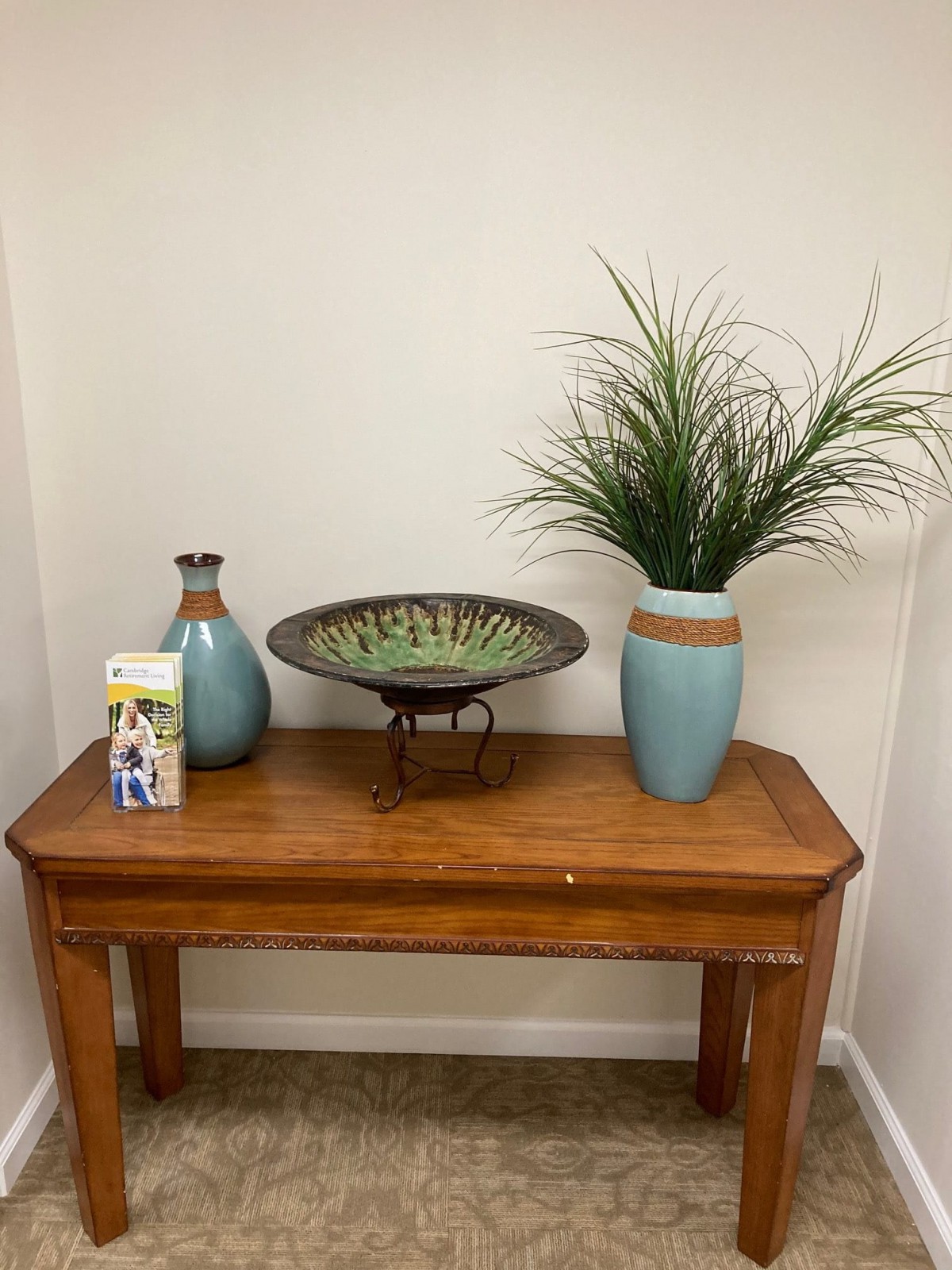 A wooden table decorated with vases, a plant, and a decorative bowl in a corner setting.