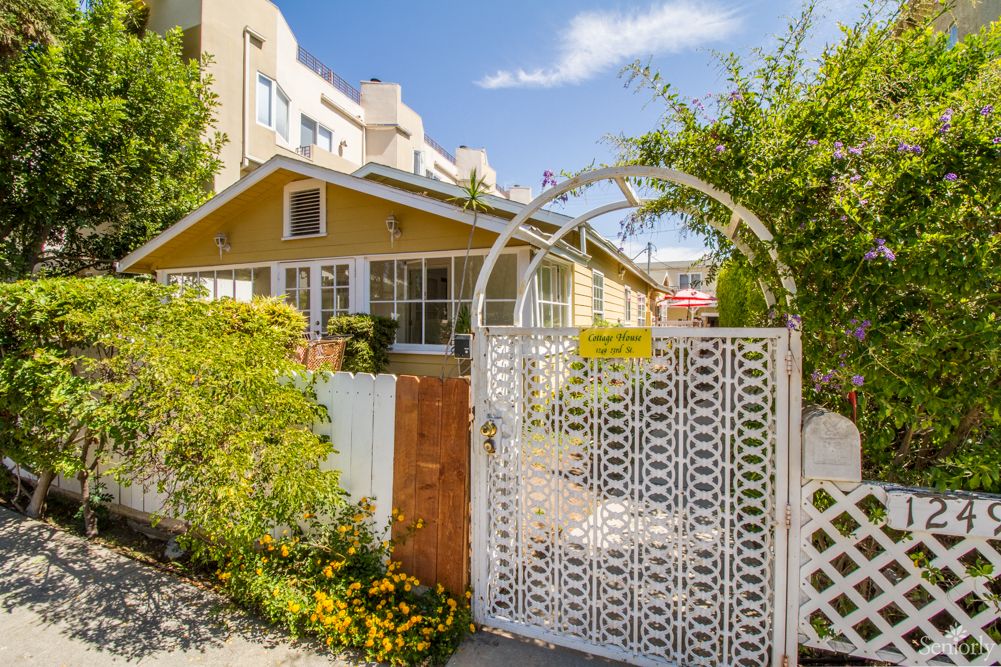A charming yellow house with a lush garden and decorative white gate under a bright blue sky.