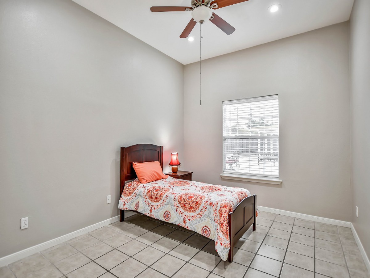 A minimalist bedroom with a single bed, a bedside lamp, and a ceiling fan.