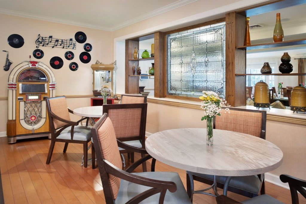 A cozy cafe interior with tables and chairs, decorated with plants and wall art.