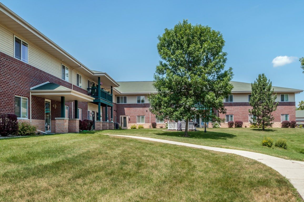 A residential apartment complex with a central courtyard featuring a tree and well-maintained grass.