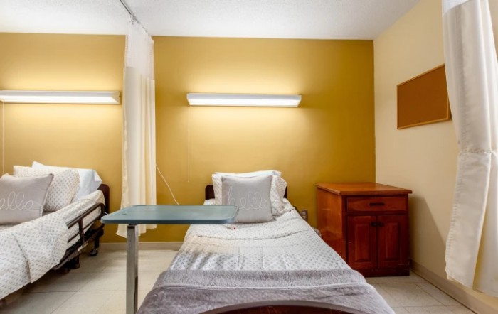 A hospital room with a neatly made bed, bedside table, and medical equipment.