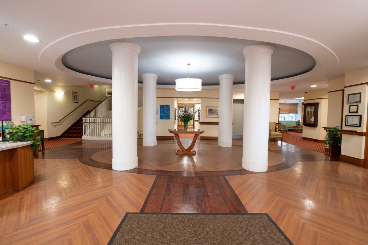 A modern lobby area with circular columns and a central wooden table, featuring elegant decor and a polished wooden floor.