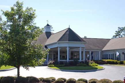 A scenic view of a building with a distinctive roof surrounded by greenery and clear skies.
